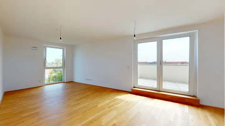 Leeres Zimmer mit hellem Holzfußboden, weißen Wänden, einem Fenster und einer Balkontür, die auf eine Terrasse führt (Arbeitergasse).