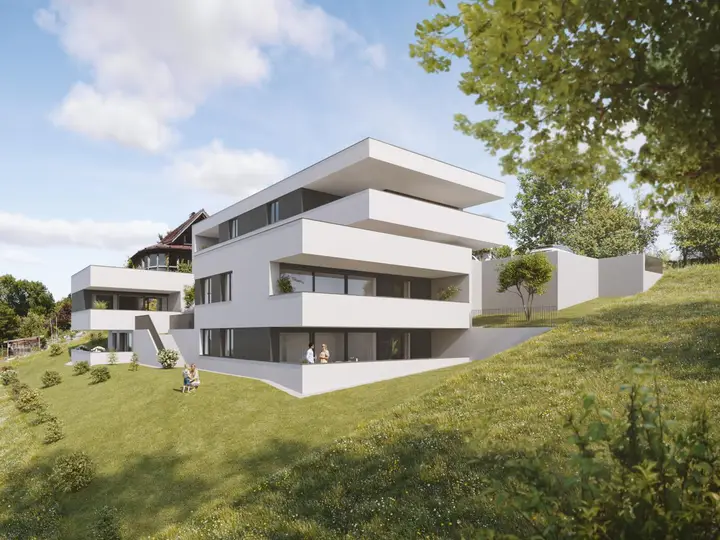 Zwei moderne weiße Wohngebäude mit Terrassen und Balkonen am Hang in Feldkirch-Rauhenweg, grüner Rasen und Bäume umgeben.