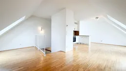 Heller offener Wohnbereich mit Dachschrägen, Holzboden und integrierter Küchenzeile.