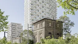 Modernes Hochhaus und historisches Gebäude in einer grünen Umgebung mit Fußgängern.