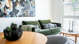 Helles Wohnzimmer mit grünem Sofa, Kunstwerk und Holztisch, modern eingerichtet.