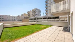Große Terrasse mit Rasenfläche und Blick auf moderne Wohngebäude.