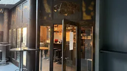 Eingangsbereich einer Bar mit rustikalen Holztüren und Glasfront, die in den Hauptraum führt.