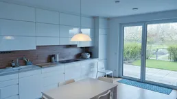 Moderne Küche mit weißen Hochglanzfronten, Holzakzenten und direktem Zugang zur Terrasse und Garten.