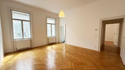 Helles Wohnzimmer mit Fischgrätparkettboden und hohen Fenstern, das viel Tageslicht hereinlässt.