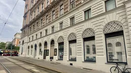 Klassisches Gebäude mit historischer Fassade und großen Bogenfenstern entlang einer Straße mit Straßenbahnschienen.