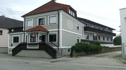 Graues Gebäude mit rotem Ziegeldach, Rollläden und einem Eingangsbereich mit Treppe.