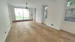 Helles Wohnzimmer mit Fischgrätparkett und großen Schiebetüren zum Gartenbereich.