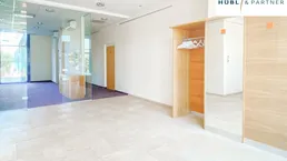 Geräumiger Empfangsbereich mit hellen Fliesen, Holzelementen und einer Garderobe, die zu weiteren Büroräumen führt.