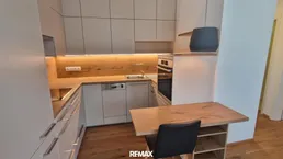 Moderne Einbauküche mit hellen Fronten, Holzakzenten und integriertem Essbereich.