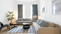 Lichtdurchflutetes Wohnzimmer mit bequemen Sofas, Holzboden und großen Fenstern.