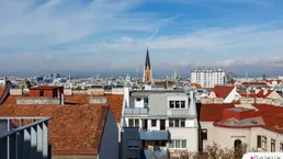 Panoramablick über die Stadt Wien mit historischen Dächern und Kirchturm unter blauem Himmel.