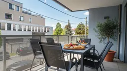Möblierter Balkon mit Esstisch und Blick auf die umliegenden Gebäude und Bäume.