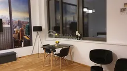 Heller Wohnbereich mit Holzboden, Esstisch und großen Fenstern, die viel Tageslicht hereinlassen.