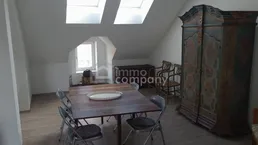 Geräumiger Essbereich im Dachgeschoss mit Holztisch, Stühlen und einem antiken Schrank unter Dachfenstern.