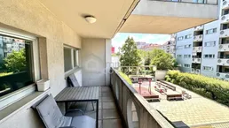 Geräumiger Balkon mit Sitzgelegenheiten und Blick auf den Innenhof mit Spielplatz.