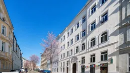 Historisches Gebäude mit weißer Fassade und vielen Fenstern an einer belebten Straße.