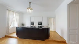 Moderne Küche mit schwarzer Kücheninsel, weißen Schränken und Fischgrätparkettboden in hellem Raum.