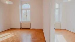 Helles Zimmer mit Parkettboden, hohen Decken und großen Bogenfenstern.