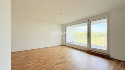 Heller Wohnraum mit Parkettboden und großem Fenster mit Zugang zum Balkon.