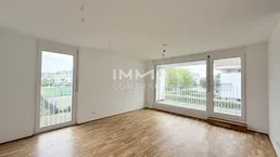 Helles Wohnzimmer mit großen Fenstern, Parkettboden und Zugang zu einem Balkon mit Weitblick.