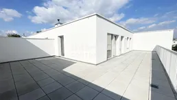 Geräumige Dachterrasse mit modernen weißen Wänden und Fliesenboden unter strahlend blauem Himmel.