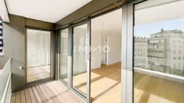 Geräumiger Balkon mit Holzboden und Glasschiebetüren, die zu einem hellen Innenraum führen.