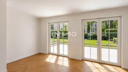 Heller Raum mit Fischgrätparkett und Zugang zu einer gepflasterten Terrasse und Garten.