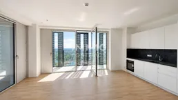 Helles, offenes Wohnzimmer mit integrierter Küche, Parkettboden und Zugang zu einem Balkon mit Stadtblick.