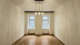 Heller, leerer Raum mit Parkettboden und zwei Fenstern, bereit zur individuellen Gestaltung.