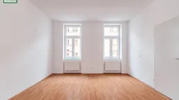 Helles Zimmer mit zwei Fenstern, weißen Wänden und Holzboden, bereit zur individuellen Gestaltung.