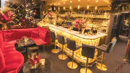 Luxuriöse Bar mit rotem Samtsofa, beleuchteter Theke und einer großen Auswahl an Getränken.
