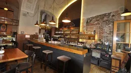 Geräumige Bar mit Holztresen, Backsteinwand und indirekter Beleuchtung unter einer Gewölbedecke.