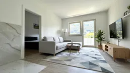 Helles Wohnzimmer mit modernem Sofa, Teppich und Bergblick durch große Fenster mit Balkonzugang.