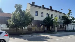 Gebäudeansicht von der Straße mit Bäumen und einem geparkten Auto vor der Fassade.