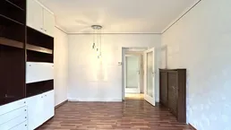 Heller Raum mit Einbauschränken, Parkettboden und Zugang zu einem weiteren Zimmer.