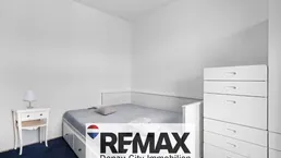 Helles Schlafzimmer mit weißem Bett und Kommode, ausgestattet mit blauem Teppichboden.