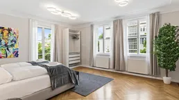 Helles Schlafzimmer mit modernem Bett, offenem Kleiderschrank und Fischgrätparkettboden.