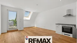 Helles Zimmer mit Holzboden, kleiner Küchenzeile, Dachfenster und Zugang zu einem Balkon.