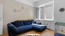 Gemütliches Wohnzimmer mit blauem Sofa, Holzboden und viel Tageslicht durch das Fenster.