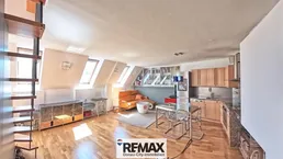 Helles Dachgeschoss-Wohnzimmer mit offener Küche, Holzboden und Dachfenstern.