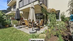 Große Terrasse mit Gartenmöbeln und Sonnenschirmen, umgeben von Grünflächen und Pflanzen.