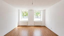 Heller, leerer Raum mit Laminatboden und zwei Fenstern, bereit zur individuellen Gestaltung.