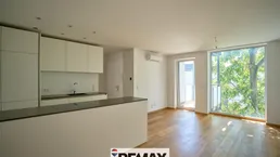 Heller offener Wohnbereich mit integrierter Küche, Parkettboden und Zugang zum Balkon.