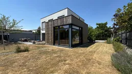 Modernes Einfamilienhaus mit Holzfassade und großem Garten unter blauem Himmel.