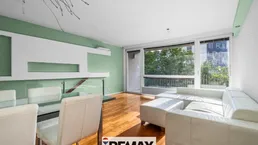 Helles Wohn- und Esszimmer mit Holzboden, weißem Sofa und Zugang zum Balkon.