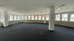 Helles und geräumiges Büro mit Teppichboden und einer Reihe von Fenstern, die den Raum erhellen und eine angenehme Atmosphäre bieten.