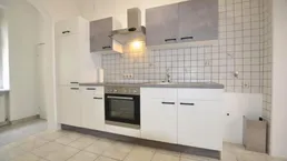 Helle Küche mit weißen und grauen Schränken, Fliesenrückwand und integriertem Backofen.