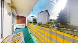 Sonniger Balkon mit gelb-grauem Sichtschutz und Blick auf die umliegenden Gebäude.