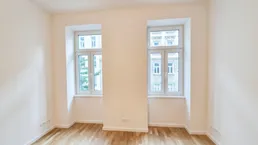 Heller Raum mit zwei Fenstern und neu verlegtem Parkettboden, ideal als Wohn- oder Schlafzimmer.